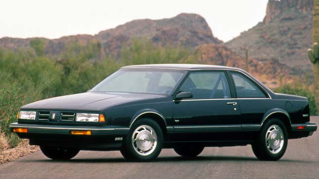 A photo of a black Oldsmobile 88 parked near a cliff. 