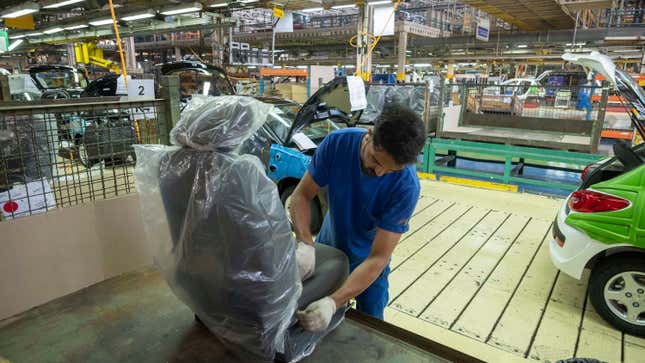 A photo inside a car manufacturing plant of a man working on a wrapped up car seat