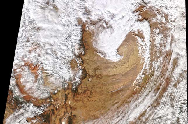A satellite view of the wind and dust storm that moved across the central U.S. in mid-December. Clouds and a large swirl of dust are clearly visible.