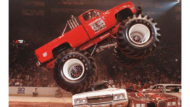 A monster truck jumps over three cars