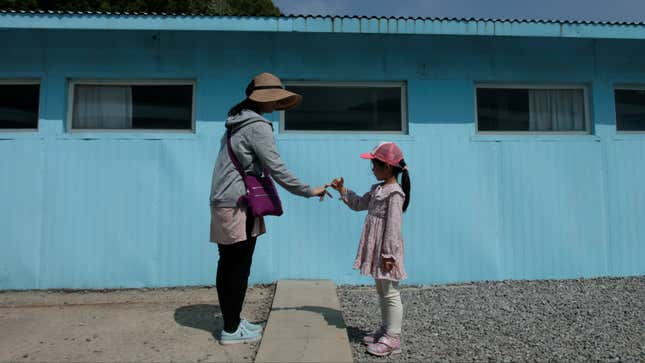 A woman and a girl shake hands over a replica of the barrier seperating North and South Korea