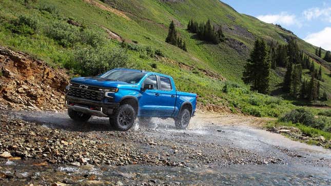 A blue Silverado driving through a creek near mountains