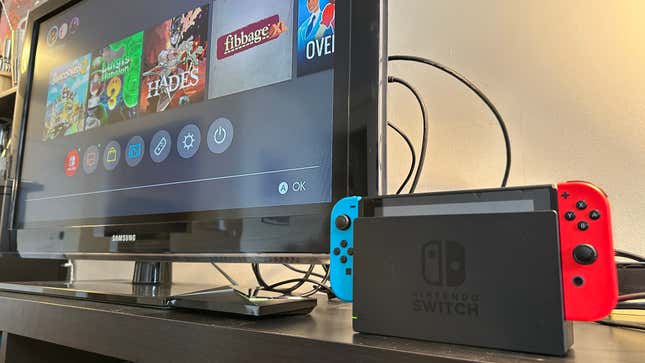 A Nintendo Switch console next to a TV showing the main screen.