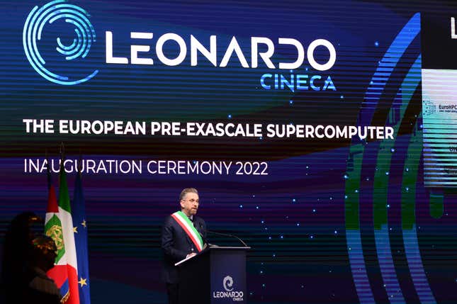 a man standing at a podium wearing a red, white, and green sash in front of a backdrop that says LEONARDO CINECA