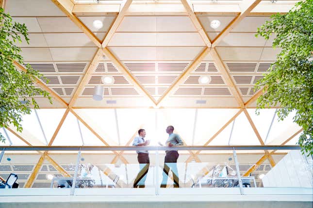 lower level view of two men work colleagues talking against a railing