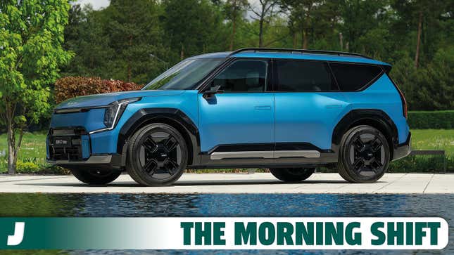 Front 3/4 angle image of a blue Kia EV9 behind a reflecting pool in a park.