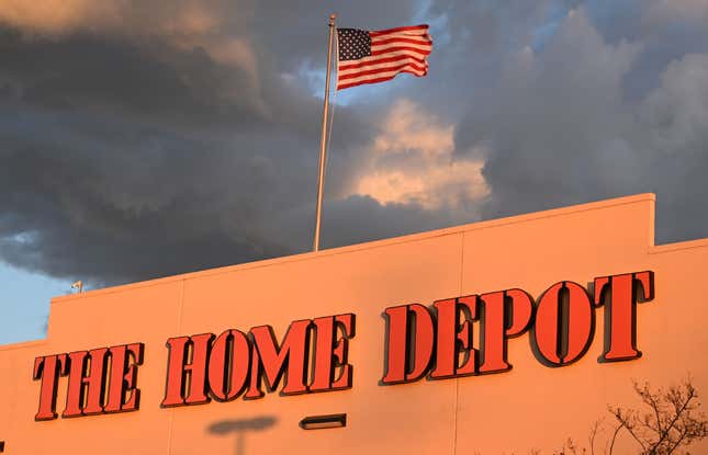 Outside of a Home Depot building with a flag on top that's waving underneath a cloudy sky