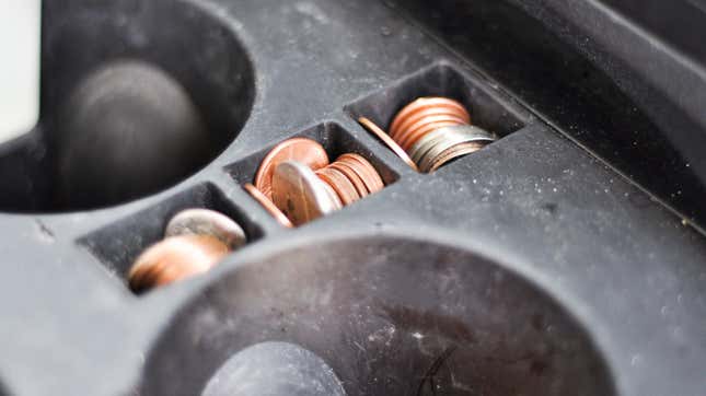 A close-up of a cup holder inside a vehicle that is very dirty. Coins sit in the coin trays. There are US pennies and nickels.