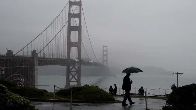 A pedestrian carries an umbrella while walking on a path in front of the Golden Gate Bridge in San Francisco on Wednesday, Oct. 20, 2021.