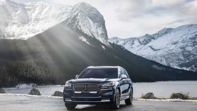 A photo of a Lincoln SUV parked near a lake. 