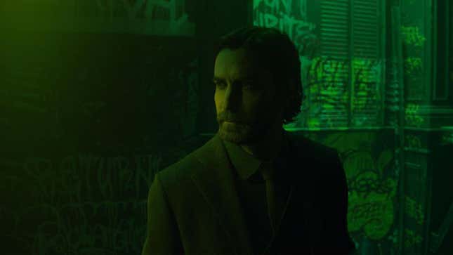 Alan Wake sits in front of a graffiti-covered wall, bathed in green light. 