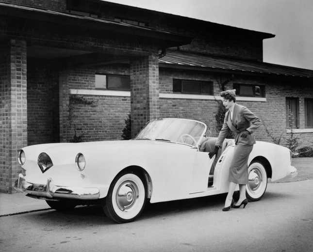 A woman slides back the driver’s door of a Kaiser Darrin, which features sliding doors, a retractable roof, and a lightweight corrosion-proof fibreglass body, Michigan, United States, 1954.