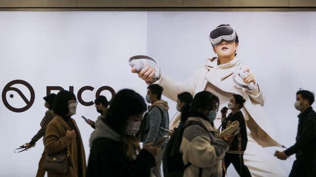 İnsanlar Pekin'deki Wangjing metro istasyonunda Douyin veya TikTok'un PICO VR kulaklığını gösteren dev ışıklı reklam kutusunun önünde yürüyor.