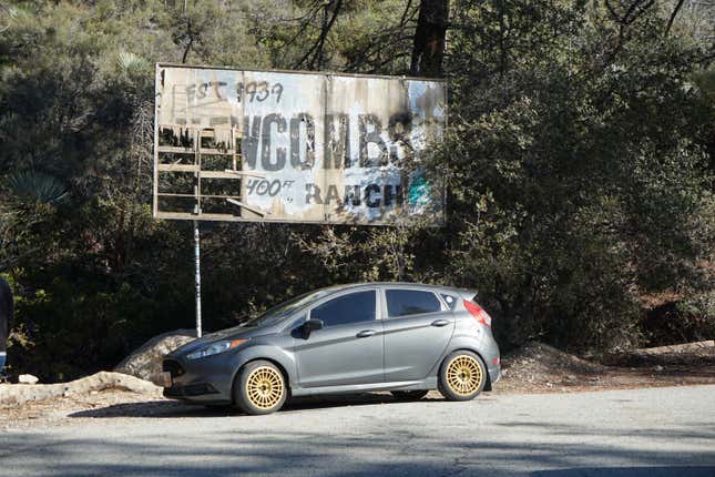 A grey 2015 Ford Fiesta ST is parked in front of a faded sign.