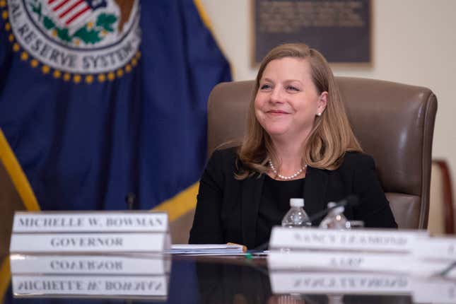 La gouverneure de la Réserve fédérale, Michelle Bowman, est assise derrière un badge nominatif flou et devant un drapeau du système de la Réserve fédérale