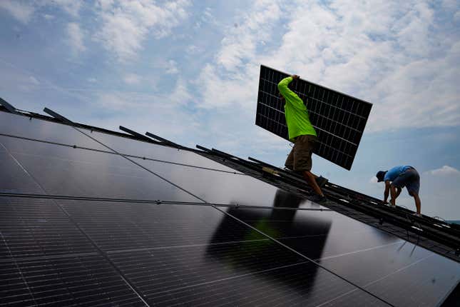 FILE - Nicholas Hartnett, owner of Pure Power Solar, carries a panel as he and Brian Hoeppner, right, install a solar array on the roof of a home in Frankfort, Ky., July 17, 2023. A business group that advocates for clean energy says at least $86 billion in investments have been announced, with the biggest likely job gains in electric vehicles, battery storage and solar energy. (AP Photo/Michael Conroy, File)