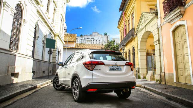 A photo of a white Honda SUV in a narrow city street. 