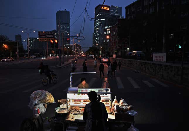 A woman buys snacks from a mobile street vendor at an intersection during rush hour in Beijing at night