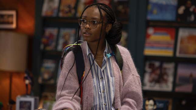 Naomi, in a striped button-down shirt and pink sweater, browses in a comic book store.