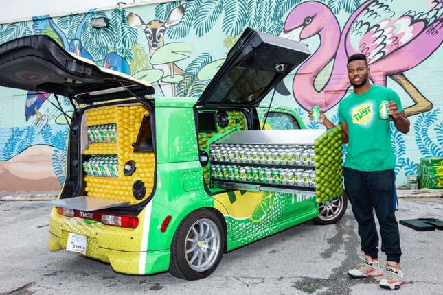 A man standing next to a custom Nissan Cube that's full of Mist Twist soda cans for promotional activities.