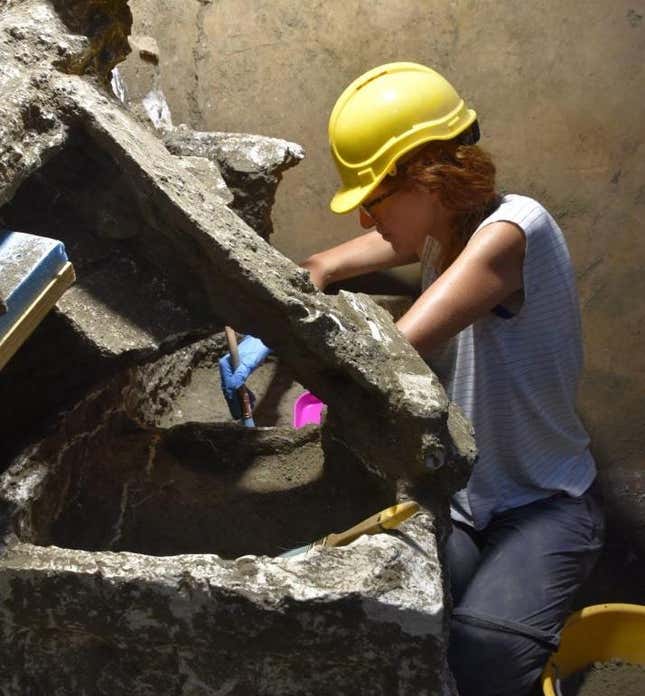 An archaeologist in a yellow hard hat works on the ashy contents of the Pompeiian chest.