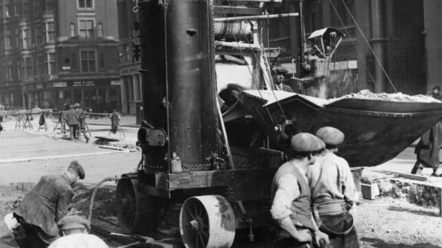 Circa 1925: Workmen repairing a road, with the aid of a cement mixer.