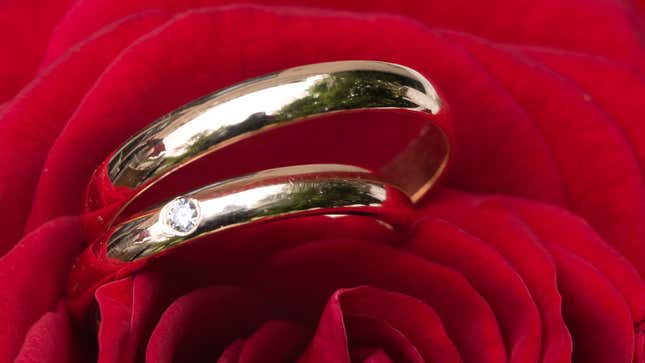 A photo of two gold wedding rings in the petals of a rose. 