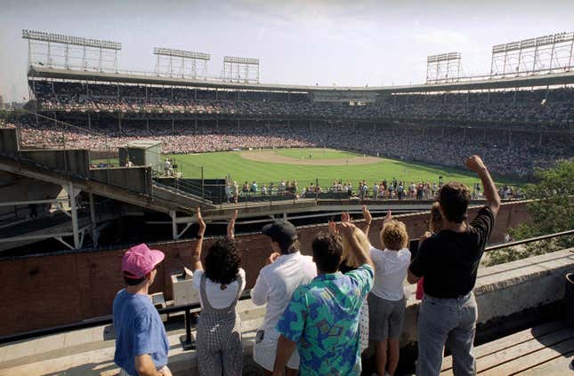 FILE - In this Monday, July 9, 1990, file photo, spectators watch an All-Star Game practice session from the roof of a building just outside Chicago&#39;s Wrigley Field. Booking hotels for baseball games during shoulder seasons like May, June or September can often be cheaper than the summer months. Additionally, save money by planning to attend weekday versus weekend games. (AP Photo/Seth Perlman, File)