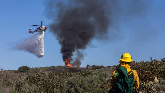 A firefighter watches as a helicopter drops water on a smoldering hillside on February 10, 2022 in Laguna Beach, California.