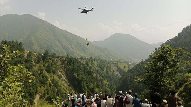 People watch as an army soldier slings down from a helicopter during a rescue mission to recover students stuck in a chairlift in Pashto village of mountainous Khyber Pakhtunkhwa province, on August 22, 2023. Six children and two adults were suspended inside a cable car dangling over a deep valley in Pakistan for several hours on August 22, as a military helicopter hovered nearby.