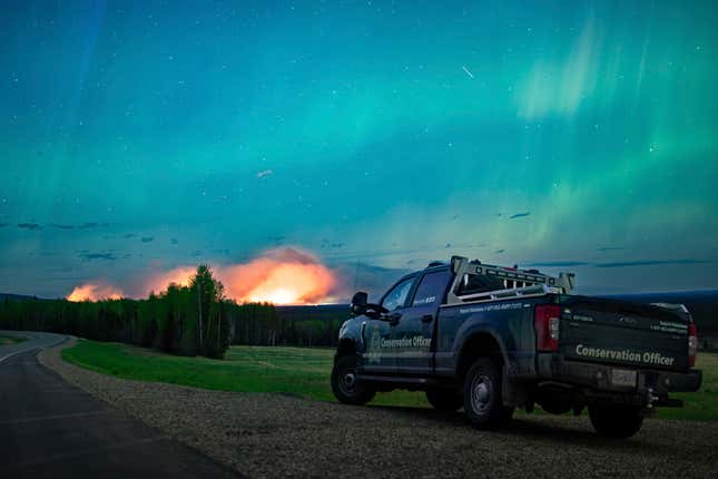 Esta foto proporcionada por el Ministerio de Agua, Tierra y Recursos muestra un incendio forestal, aurora boreal en lo alto, cerca de Fort Nelson, británico  Columbia sábado 11 de mayo de 2024. 