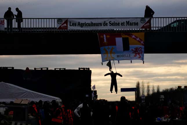 Farmers gather under a bridge where hangs a dummy farmer as farmers block a highway Tuesday, Jan. 30, 2024 in Jossigny, east of Paris. With protesting farmers camped out at barricades around Paris, France&#39;s government hoped to calm their anger with more concessions Tuesday to their complaints that growing and rearing food has become too difficult and not sufficiently lucrative. (AP Photo/Christophe Ena)