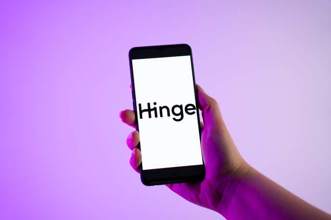 A person is holding a mobile phone with the Hinge dating app logo on its screen.