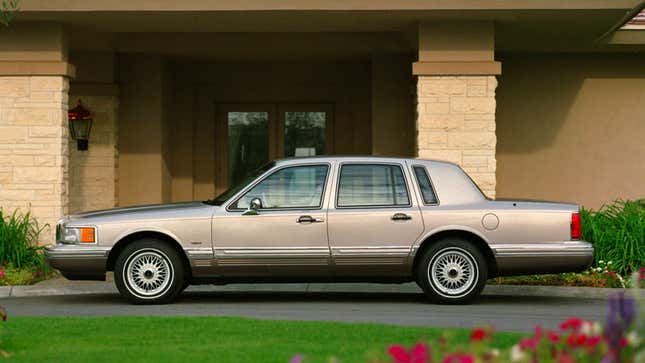 A photo of a silver Lincoln Town Car sedan parked in front of a house. 