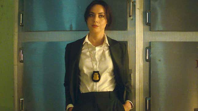 Aubrey Plaza dressed as a government agent stands in a morgue