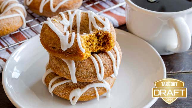 Stack of three pumpkin spice doughnuts with icing drizzle on a white plate beside a mug of coffee