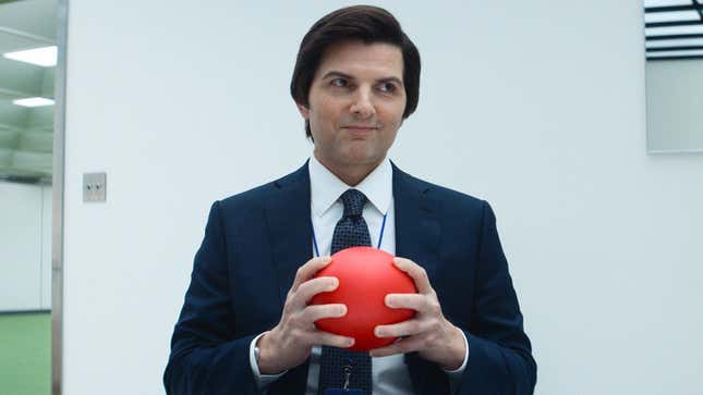 Adam Scott is wearing a blue blazer and tie, holding a red ball.