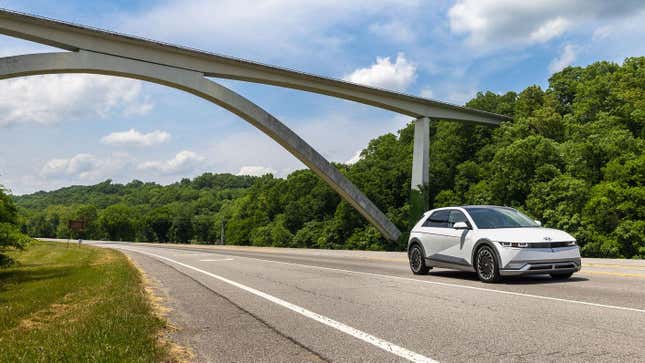 Un Ioniq 5 blanco conduciendo delante de un puente y muchos árboles