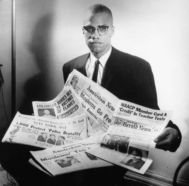 Malcolm X reading stories about himself in a pile of newspapers, circa 1963.