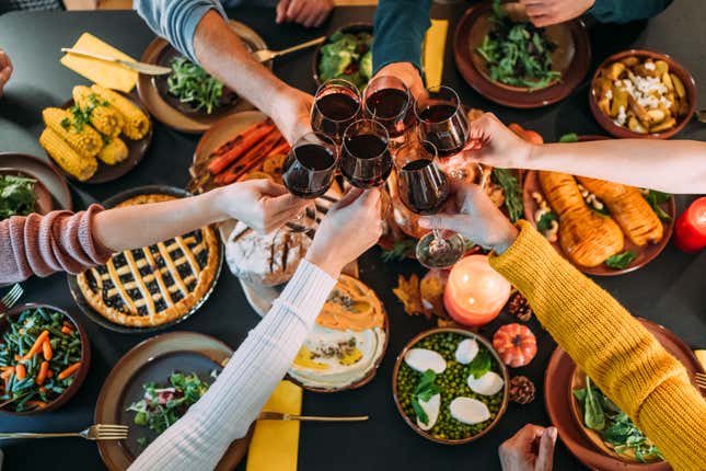 Above view of happy multi-generation family gathering for Thanksgiving meal at dining table. Shot of group of unrecognizable people toasting with wine during Thanksgiving or Christmas dinner or lunch.