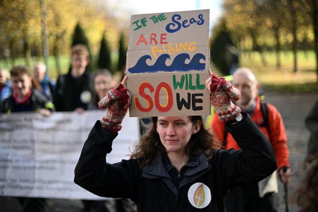 A woman holds up a placard at the start of a "Pilgrims Procession" an opening ceremony to a series of non-violent direct actions being organised by the Extinction Rebellion climate activist action group near the Scottish Event Centre (SEC) in Glasgow, Scotland on October 30, 2021, venue of the COP26 UN Climate Change Conference to be held in the city from October 31. - Pilgrimage groups and artists, including members of XR Faith, are walking to Glasgow to raise awareness of the climate crisis and demand a fair deal at COP26 for the Global South as Britain hosts more than 120 leaders in Glasgow, before the UN meeting spends a fortnight tackling the work of deciding how to limit temperature rises to 1.5 degrees Celsius. (Photo by DANIEL LEAL-OLIVAS / AFP) (Photo by DANIEL LEAL-OLIVAS/AFP via Getty Images)