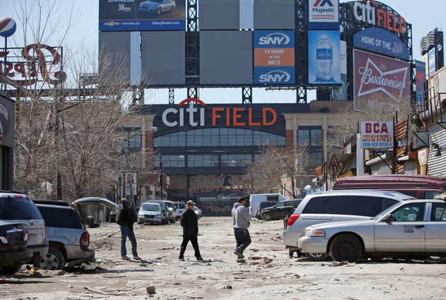 FILE - In this April 2, 2015 photo, workers cross an unpaved street adjacent to Citi Field, home to the New York Mets baseball team in the Willets Point section of the Queens borough of New York. New York City officials approved a plan Thursday, April 11, 2024, to build a 25,000-seat stadium for Major League Soccer’s New York City Football Club next to the New York Mets’ stadium, Citi Field. The $780 million soccer stadium, expected to open in 2027, will anchor a 23-acre redevelopment project in the neighborhood known as Willets Point that will also include housing, a new public school, retail stores and a hotel. (AP Photo/Kathy Willens, File)