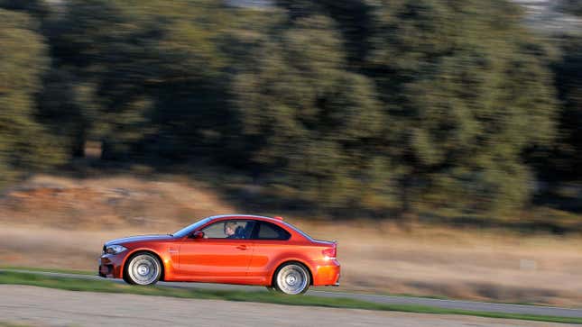 A bright orange BMW 1M driving in front of trees