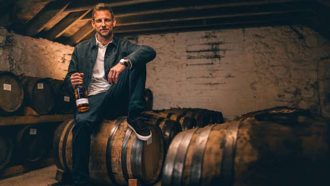 A photo of Jenson Button sat on a barrel of whisky. 