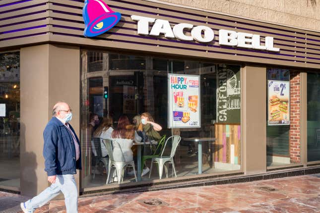 Un homme portant un masque passe devant un restaurant Taco Bell. 