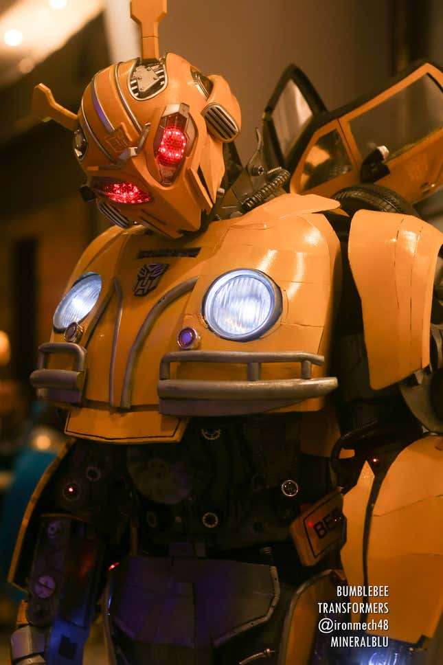 A cosplayer dressed as Bumblebee from Transformers cocks their head at the camera.