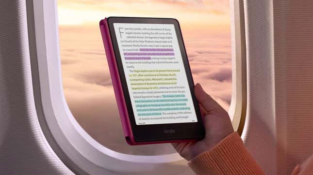 Persona sosteniendo un Kindle Colorsoft con una cubierta rosa y texto resaltado (en rosa, amarillo y azul) frente a la ventana de un avión mirando hacia el amanecer