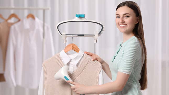 A woman steams a sweater vest over a button-down shirt. 