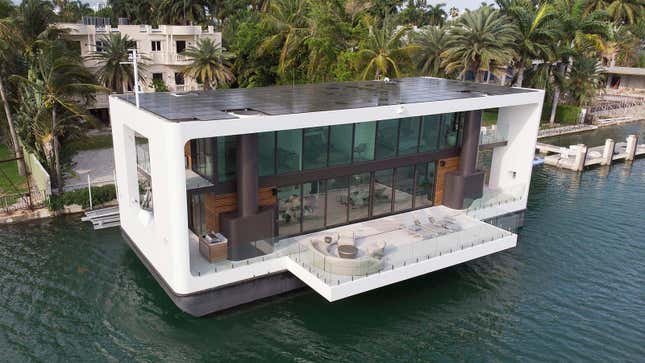 A large white floating houseboat is tied to the shore