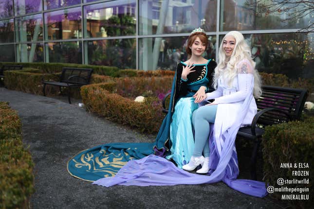 Anna and Elsa cosplayers sit together on a bench. 